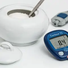 Cukiernica z łyżeczką, glukometr i nakłuwacz na białym tle.