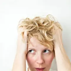 Zmartwiona kobieta z blond włosami, która trzyma się za głowę. Czy to objaw choroby?