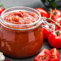 Słoik domowego sosu pomidorowego, bogatego w likopen, otoczony świeżymi pomidorami, czosnkiem i papryczkami chili.