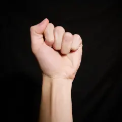 Zaciśnięta pięść, widoczna od nadgarstka w górę. Palce, choć zgięte, wydają się krótsze, co może sugerować brachydaktylię.