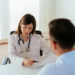 Lekarka omawia z pacjentem zwolnienie lekarskie po ustaniu zatrudnienia, wskazując na dokument.