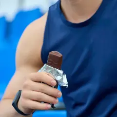 Mężczyzna w niebieskiej koszulce sportowej trzyma batonik. To szybkie źródło energii, które pomoże uzupełnić zapasy glikogenu po treningu.