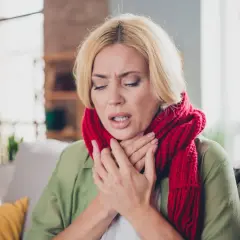 Kobieta z czerwoną szalikiem na szyi, z bólem gardła, może to być objaw dyfterytu.
