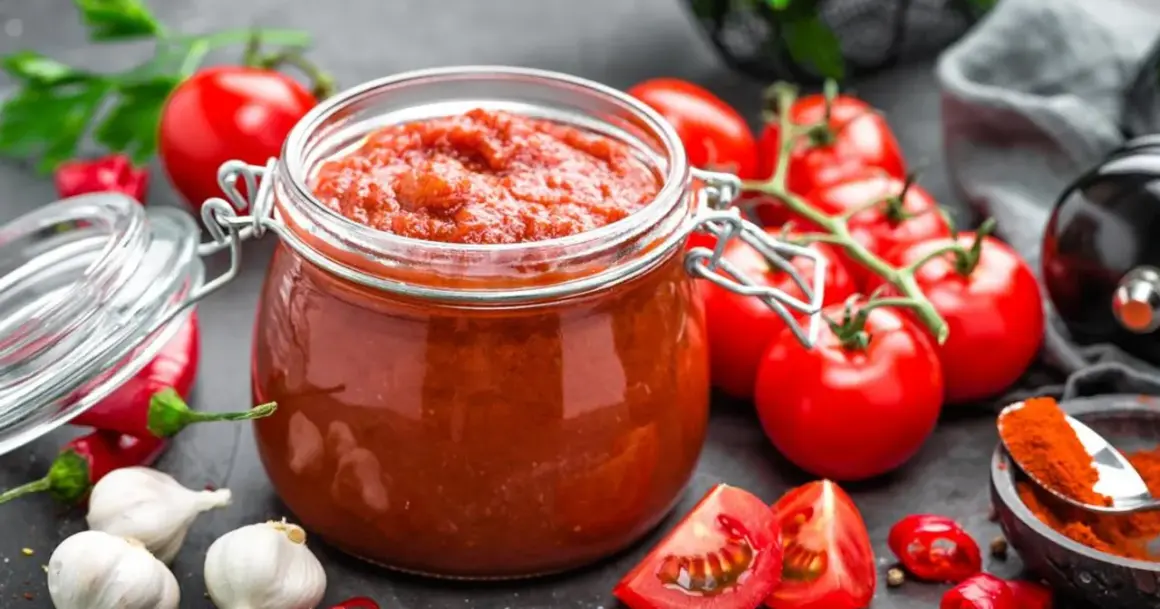 Słoik domowego sosu pomidorowego, bogatego w likopen, otoczony świeżymi pomidorami, czosnkiem i papryczkami chili.