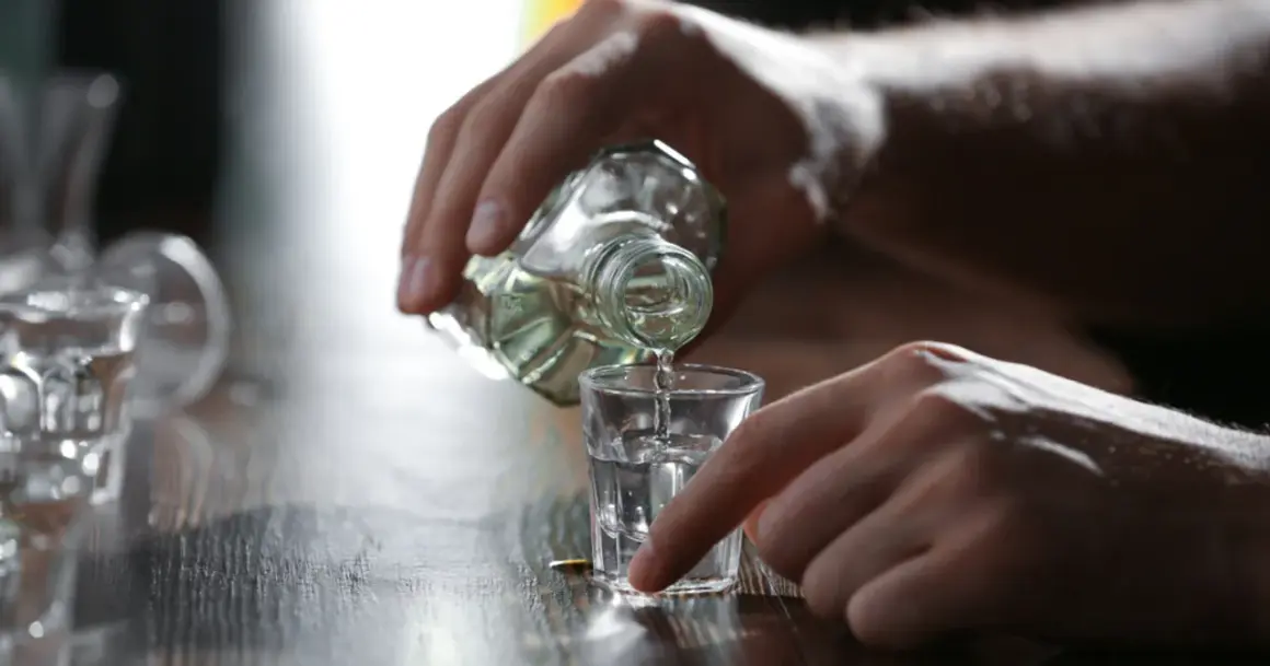 Dłoń nalewa alkohol do kieliszka. Może to być pierwszy kieliszek wypity na czczo.